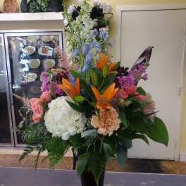 Tall mixed flower arrangement in a black vase with lilies, hydrangea, and roses