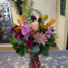 Colorful mixed bouquet in a pink glass vase with lilies, roses, and chrysanthemums