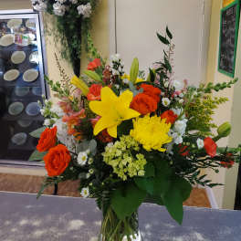 Mixed bouquet with yellow lilies, orange roses, and white daisies in a glass vase