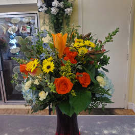 Mixed bouquet with orange roses, yellow daisies, and lilies in a dark vase