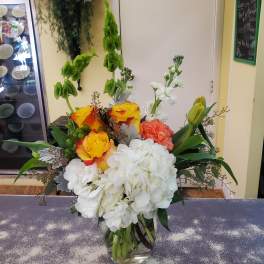 Colorful bouquet with white hydrangeas, yellow roses, and green tulips in a glass vase