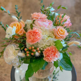 Peach and white bouquet with roses, carnations, and hydrangea in a glass vase