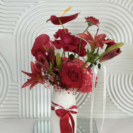 Red floral arrangement in a white vase with a ribbon bow