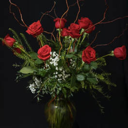 Red roses arranged in a glass vase with curly branches