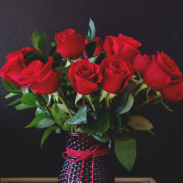 Red roses arranged in a textured vase with a red cord and heart charm