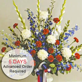 Tall red, white, and blue flower arrangement in a white vase with patriotic ribbon bow