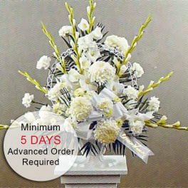 Tall white funeral-style flower arrangement on a pedestal with a white bow.