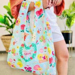 Reusable pastel tote bag with cute floral and character illustrations held by a person indoors