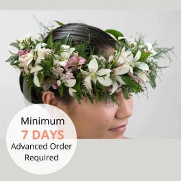 White and pink flower crown with lush foliage worn around a woman's head.