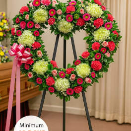 Heart-shaped standing wreath with green hydrangeas, pink roses, and bright pink flowers on a black easel.