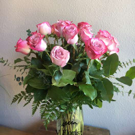Tall arrangement of pink roses in a clear glass vase on a wooden surface