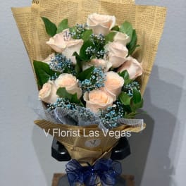 Bouquet of pale peach roses with blue filler flowers in newspaper-style wrap