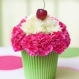 Cupcake-shaped flower arrangement with pink and white blooms topped by a cherry