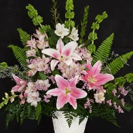 Pink lilies and small white flowers arranged in a white vase