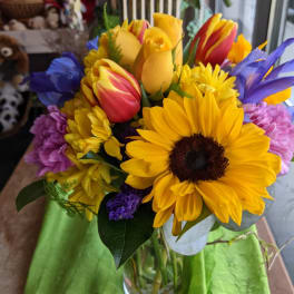 Bouquet of sunflowers, tulips, and purple flowers in a glass vase