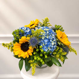 Sunflowers and blue hydrangeas arranged in a clear glass vase