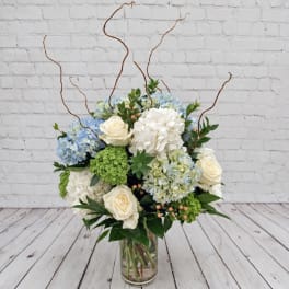 Blue and white floral arrangement in a clear glass vase with curly branches