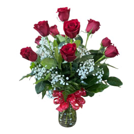 Arrangement of red roses with white filler flowers in a clear glass vase with a red bow