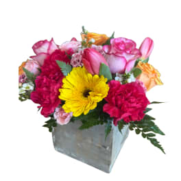 Mixed pink and yellow flowers in a square metal vase