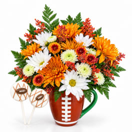 Football-shaped mug filled with orange and white flowers, with two football cake pops beside it