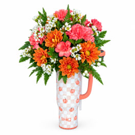 Bouquet of pink and orange flowers in a pumpkin-patterned tumbler