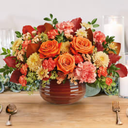 Orange roses and mixed blooms in a brown vase on a table