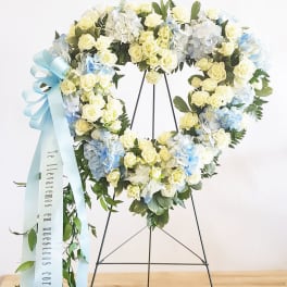 Heart-shaped floral wreath with pale roses, hydrangeas, and a blue ribbon