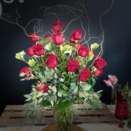 Tall bouquet of red roses in a glass vase with curly branches
