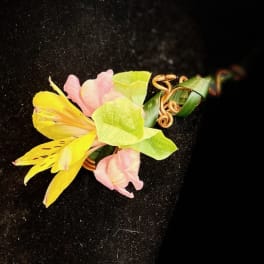 Small floral corsage with yellow and pink blooms on a black background