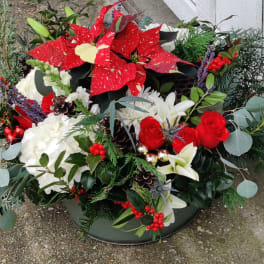 Holiday floral arrangement with red poinsettias, white blooms, and berries in a low container