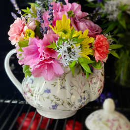 Pink and yellow flowers arranged in a floral teapot vase