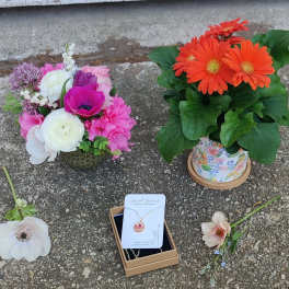 Two flower arrangements and a necklace gift box on pavement.