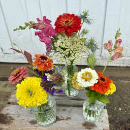 Three small flower arrangements in clear glass vases with bright mixed blooms