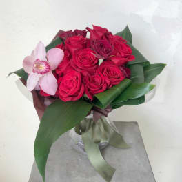 Bouquet of red roses with a pink orchid and broad green leaves