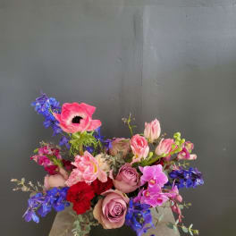 Mixed bouquet with pink roses, blue delphinium, and orchids in a black vase