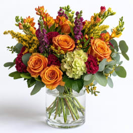 Orange roses and mixed flowers arranged in a clear glass vase