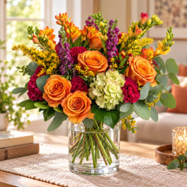Orange roses and mixed blooms in a clear glass vase