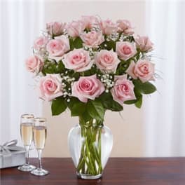 Pink rose bouquet in a clear glass vase beside two champagne flutes