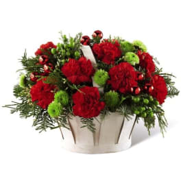 Red carnations and green pom-poms in a white basket with holiday ornaments.