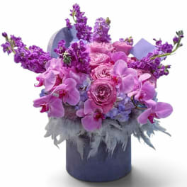 Pink roses and purple orchids arranged in a blue hatbox