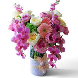 Pink and white floral arrangement in a wrapped glass vase with orchids and roses.