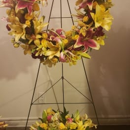 Large floral wreath on a black stand with yellow lilies and pink flowers