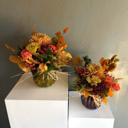 Two autumn floral arrangements in glass vases on white pedestals