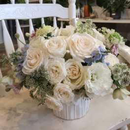Cream rose bouquet in a white vase with small blue and green accent flowers