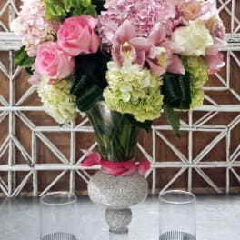 Pink and white floral arrangement in a glass vase with two candle holders