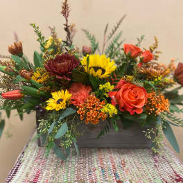 Mixed floral arrangement in a rectangular wooden container with orange and yellow blooms