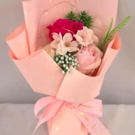 Small bouquet of pink and white roses and blossoms wrapped in pale pink paper with a bow