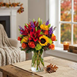 Mixed bouquet of lilies, roses, sunflowers, and purple filler in a glass vase