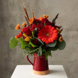 Red and orange mixed bouquet in a red ceramic pitcher