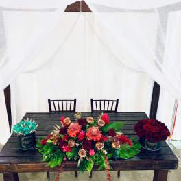 Three floral arrangements on a table, including red roses and turquoise roses in black containers